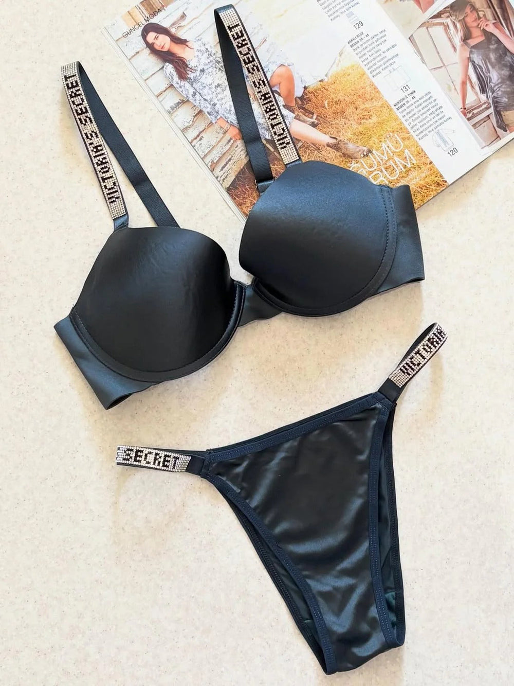 Black Victoria's Secret lingerie set on a textured surface with a magazine in the background.